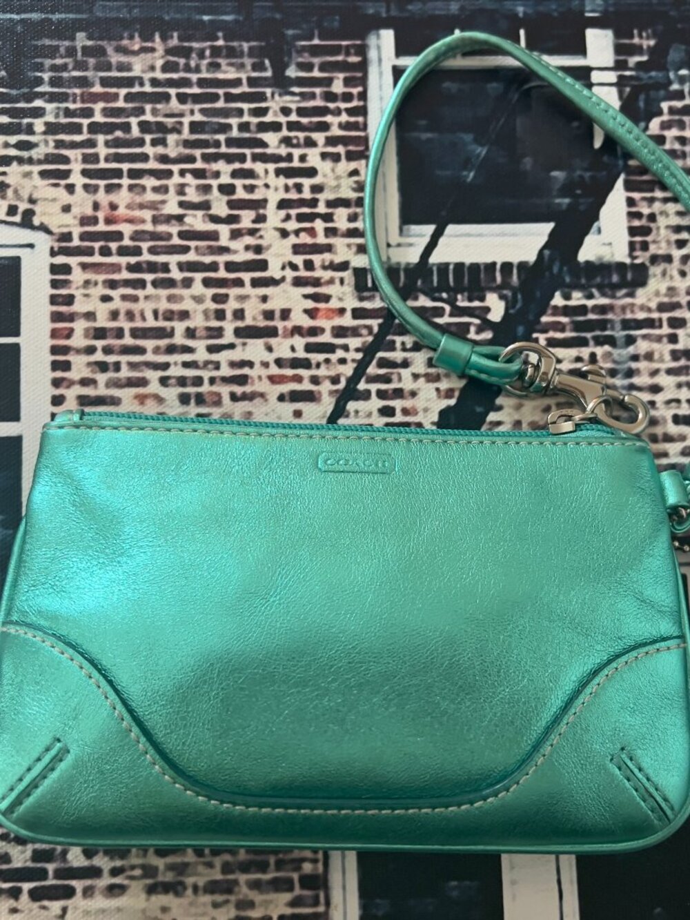 green Coach wristlet features metallic leather and a convenient wrist strap